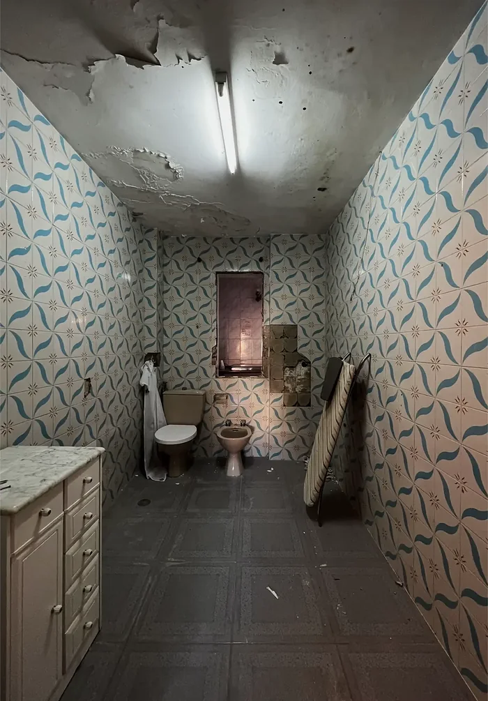 Baño antiguo antes de la reforma, con azulejo azul y techo desconchado
