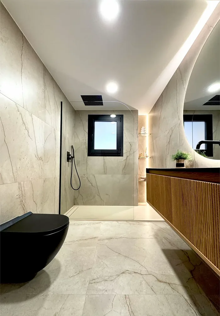 Baño reformado con porcelánico efecto mármol, mueble de madera y espejo LED