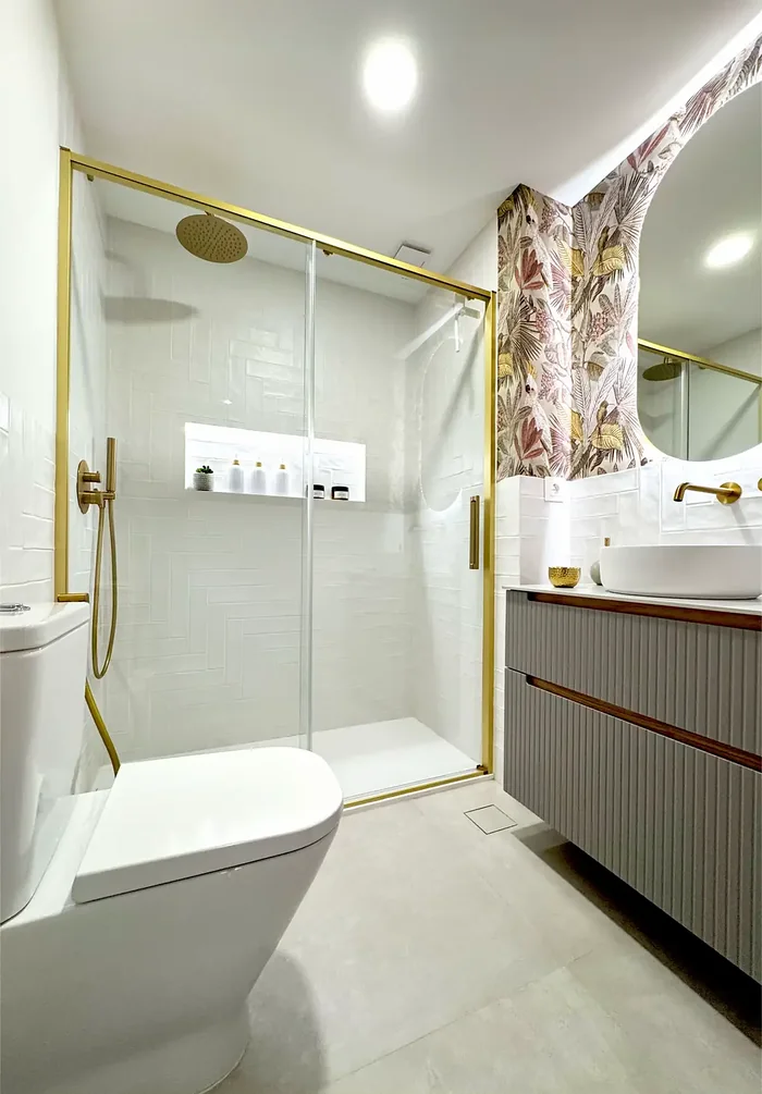 Baño reformado con ducha de mampara dorada y papel tropical