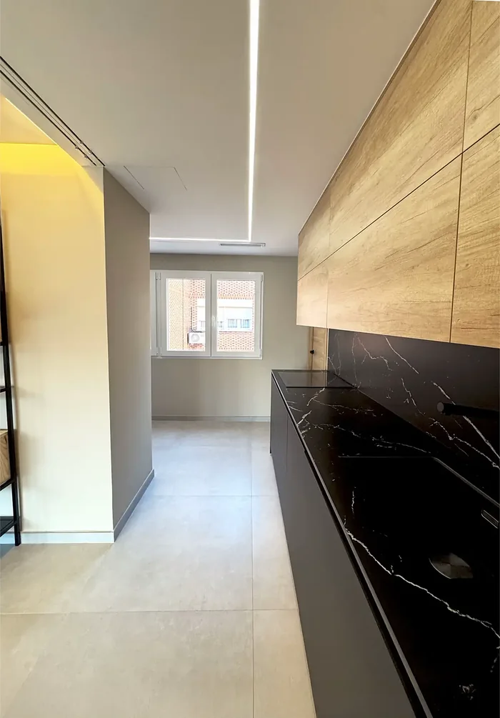 Cocina reformada con muebles de madera, encimera de piedra negra y línea LED